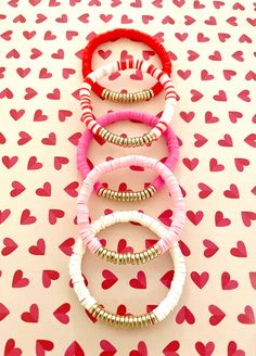 four bracelets with red and white hearts on a pink background that has gold colored beads