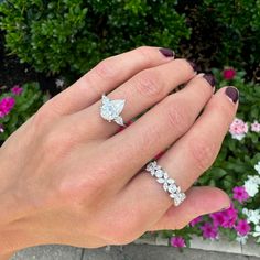 a woman's hand with two rings on it and flowers in the back ground