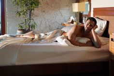 a man laying on top of a bed next to a plant in a room with stone walls