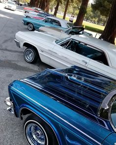 several classic cars parked in a row on the side of the road near some trees