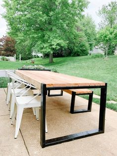 a long wooden table sitting on top of a cement ground next to a lush green park