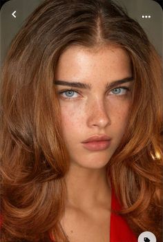 a woman with freckled hair and blue eyes looks at the camera while wearing a red top