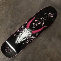 a black skateboard with pink and white designs on the bottom, sitting on concrete