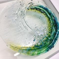 a glass plate with green, blue and yellow designs on the rim sitting on a white surface