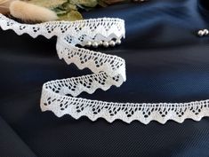 two pieces of white lace on a black cloth with beads and flowers in the background