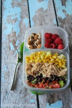 a plastic container filled with food on top of a wooden table next to a fork and knife