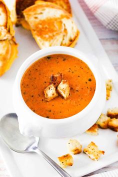 a white plate topped with a bowl of soup and croutons