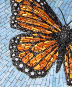 a butterfly made out of orange and black beads on a blue mosaic tile background with white dots