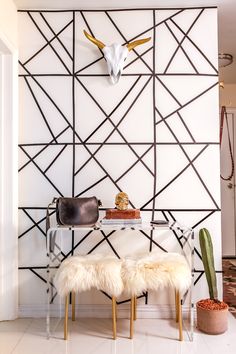 a white table topped with two stools next to a wall covered in geometric art