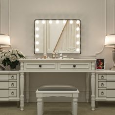 a white vanity with lights on it and a bench in front of the mirror that is lit up