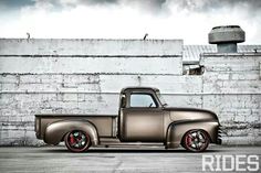 an old silver truck parked in front of a white brick wall with red rims