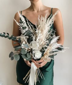 a woman in a green dress holding a bouquet of white flowers and greenery on her arm