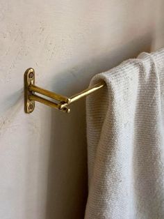 a towel hanging on the side of a white wall next to a metal hook with two gold handles