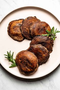 three pieces of steak on a white plate with green garnish and sprigs