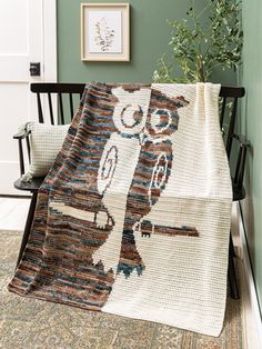 an owl afghan is sitting on a chair next to a potted plant and framed pictures