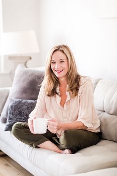 a woman sitting on top of a white couch holding a coffee cup in her hand