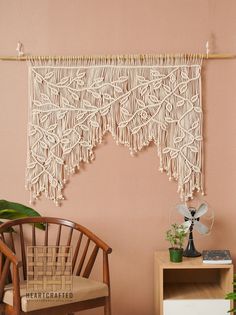 a room with a chair, table and macrame wall hanging on the wall