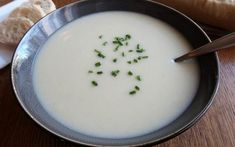 there is a bowl of soup on the table with bread in the background and a glass of milk next to it