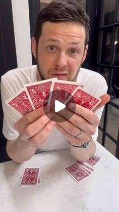 a man sitting at a table with four playing cards in front of his face and the other hand holding one