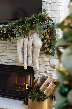 stockings hanging from a mantel with greenery and pine cones on it in front of a fireplace