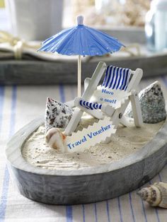 a miniature beach chair and umbrella on a tray with shells, sand and seashells