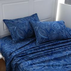 a bed with blue sheets and pillows on top of it next to a white headboard