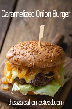 a cheeseburger with lettuce and onions on a wooden board that says caramelized onion burger