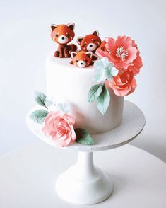 a white cake with pink flowers and two little foxes on top