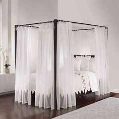 a canopy bed with sheer curtains over it in a white and black bedroom, along with hardwood flooring