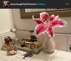 a pink flower sitting in a white vase on top of a counter next to jewelry