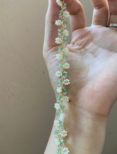 a woman's hand holding a bracelet with flowers and pearls attached to the wrist