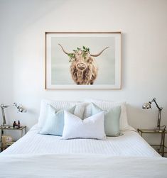 a white bed topped with lots of pillows under a framed animal print on the wall