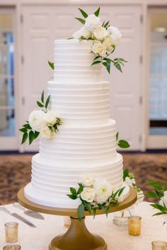 a wedding cake with white flowers and greenery on the top tier is sitting on a table