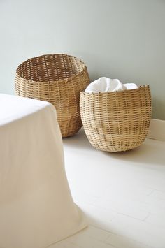 two wicker baskets sitting on the floor next to a white tablecloth covered bed