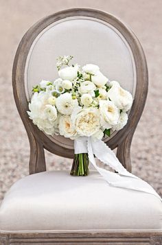 a bouquet of white flowers sitting on top of a chair in front of gravel ground