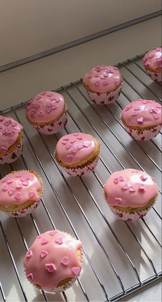 pink frosted cupcakes sitting on top of a cooling rack