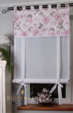 a window with pink roses on the valance and white ribbon hanging from it's side