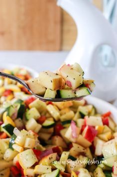 a spoon full of chopped vegetables on top of a white bowl with a fork in it