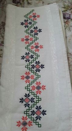 a cross stitched table runner with flowers and leaves on the border, sitting on a bed