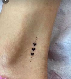 small black hearts tattoo on the side of a woman's ankle, with tiny dots