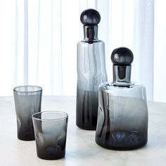 three glass vases sitting on top of a table next to two glasses and a bottle