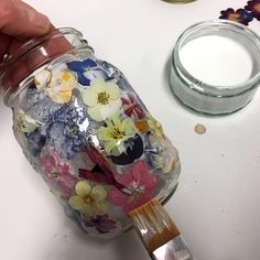 a person painting flowers on a jar with a paintbrush and some other items nearby