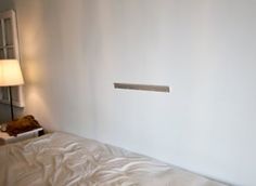 a bed with white sheets and a lamp on the wall next to it's headboard