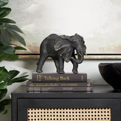 an elephant figurine on top of two books in front of a potted plant