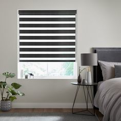 a bed room with a neatly made bed and a large window covered in blind shades