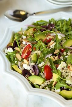 a salad with tomatoes, avocado, olives and feta cheese in a white bowl