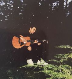 a man sitting in the grass playing a guitar