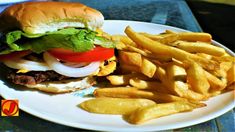 a hamburger with lettuce, tomato and onion next to french fries on a plate