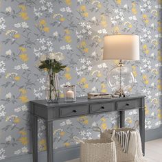 a grey table with flowers on it in front of a wallpapered background and a lamp