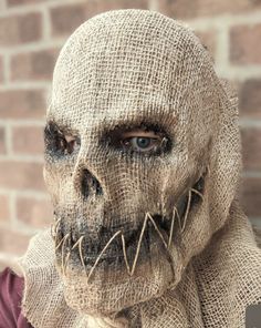 a creepy looking person wearing a burlap cloth mask with sharp teeth and fangs